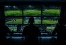 Ilustracyjna grafika piłkarska przedstawiająca abstrakcyjny pokój wideo z monitorami i sylwetkami arbitrów analizujących sporną sytuację.