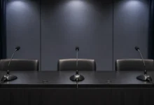 Ilustracyjna grafika piłkarska przedstawiająca pusty stół z mikrofonami przed konferencją prasową, bez logotypów i napisów.