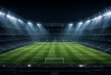 Ilustracyjna grafika piłkarska przedstawiająca pustą murawę oświetloną stadionowymi reflektorami w neutralnej scenie.